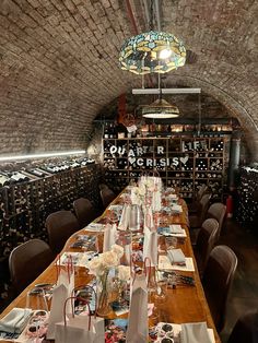 a long wooden table with many place settings on it in a wine cellar filled with bottles and glasses