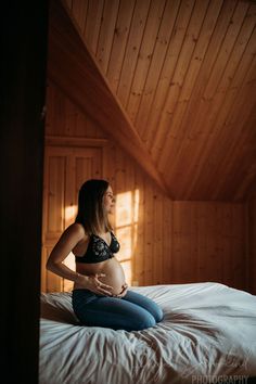 a pregnant woman sitting on top of a bed in a room with wood paneled walls