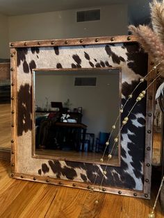 a cow print mirror sitting on top of a wooden floor next to a vase filled with flowers