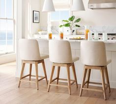 three chairs sitting in front of a kitchen island with white counter tops and wooden legs