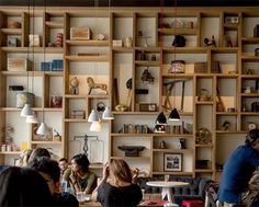 several people sitting at tables in a room with bookshelves and lamps on the wall