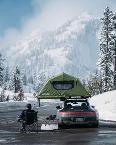 a man sitting in a chair next to a car with a tent on top of it