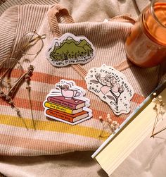 some stickers are laying on top of a blanket next to a book and glasses