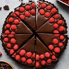 a chocolate cake with raspberries on top is cut into eight slices and sits next to other desserts