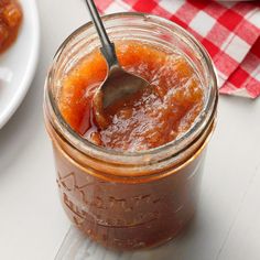 a spoon in a jar filled with jam on a table next to plates and utensils