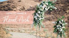 a wedding arch decorated with white flowers and greenery in front of a mountain range