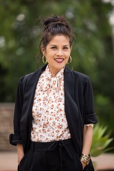 a woman wearing black pants and a white blouse smiles at the camera with trees in the background