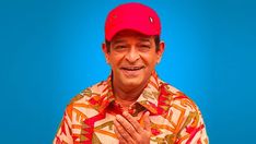 a man in a hawaiian shirt and red hat with his hands folded up to the side