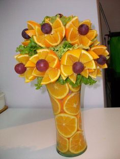 a vase filled with oranges and grapes