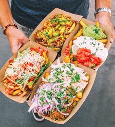 a man holding three trays filled with different types of food on top of each other