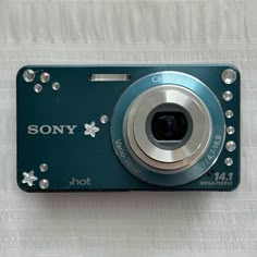 a compact camera sitting on top of a white cloth covered tablecloth with the words sony printed on it