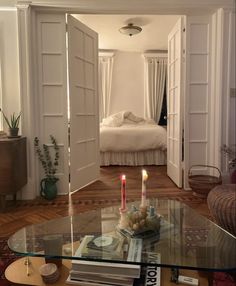 a living room filled with furniture and a glass coffee table topped with candles next to a bed