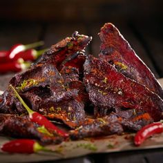 several pieces of meat sitting on top of a wooden cutting board next to red peppers