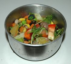 a metal bowl filled with vegetables on top of a table