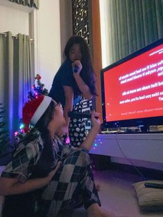 two people sitting on the floor in front of a television with a christmas hat on