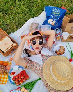 a woman laying on top of a white blanket next to picnic foods and drinks in baskets