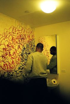 two men standing in front of a mirror with graffiti on the wall next to them