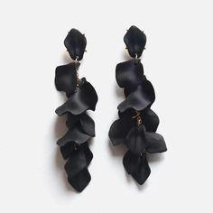 two pairs of black flower earrings on a white surface, with one pair dangling from the back