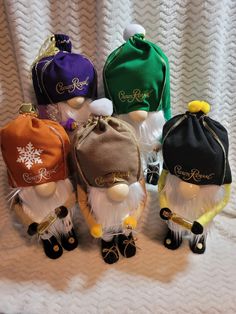 six small hats are lined up on a white blanket, one is wearing a hat and the other has an ear flap