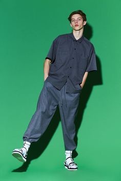 a young man standing in front of a green background wearing an oversize shirt and pants