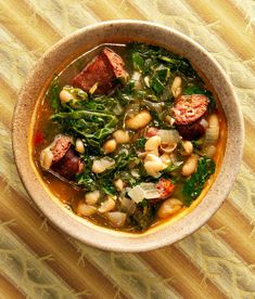 a bowl of soup with sausage, beans and spinach on a striped tablecloth