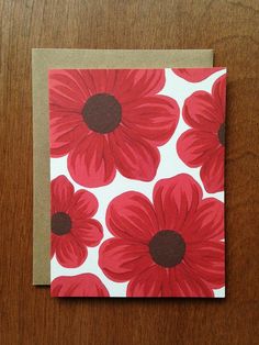 a card with red flowers on it sitting on top of a wooden table next to a pen