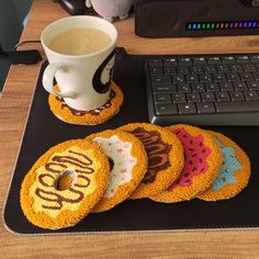 four decorated donuts sitting on top of a desk next to a cup of coffee