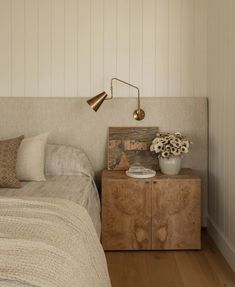 a bed room with a neatly made bed next to a night stand and flower vase