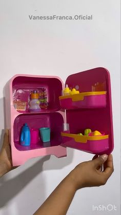 a hand holding a pink toy refrigerator with food in it's door and shelves