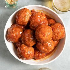 a white bowl filled with meatballs covered in sauce next to glasses and utensils