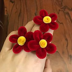 two red flowers with yellow centers are held in someone's hand on a wooden table