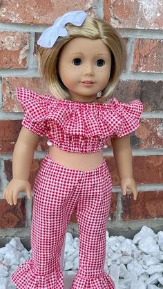 a doll with blonde hair wearing red and white checkered pants, top and headband standing in front of a brick wall