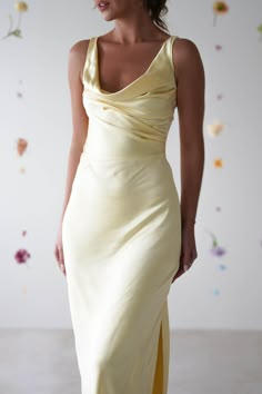 a woman in a long yellow dress with flowers on the wall behind her is looking back at the camera