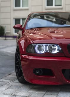 the front end of a red sports car parked on a brick sidewalk in front of a building