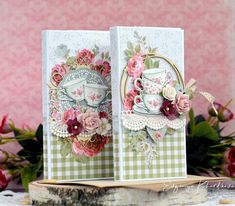 two cards with flowers on them are sitting on a table next to some pink roses