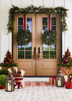 two christmas wreaths on the front door of a house with holiday decorations around them