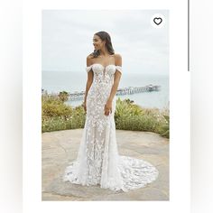 a woman in a white wedding dress standing on a stone patio next to the ocean