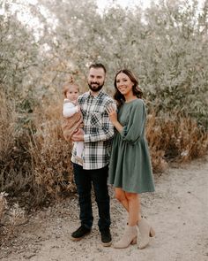 a man and woman holding a baby standing in front of some bushes with tall grass