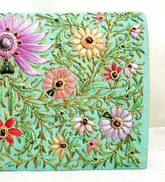 "Stunning one-of-a-kind statement clutch, a lush garden of glowing silk flowers hand embroidered on a rich turquoise/green silk background, and embellished with metallic threads and genuine star ruby stones. The sumptuous luster of silk and the exquisite embroidery make this a show stopping purse! The lotus flower is a symbol of rebirth and new beginnings - perfect for weddings and life's transitions. The word Zardozi means \"gold thread\". It is an elaborate and intricate embroidery using metal Elegant Green Bag With Floral Embroidery, Elegant Green Bags With Floral Embroidery, Green Clutch For Festival Gifts, Green Clutch For Festive Occasions, Green Festive Clutch As A Gift, Handmade Green Clutch For Festivals, Green Bags With Floral Embroidery As A Gift, Luxury Embroidered Green Bag, Luxury Green Embroidered Bag