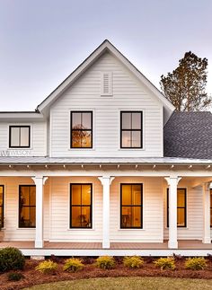 a white two story house with large windows and columns on the front porch is shown