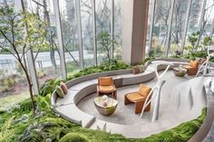 a room filled with lots of green plants and couches next to large glass windows