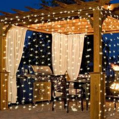 a gazebo covered in lights and curtains next to a fire pit with an outdoor grill