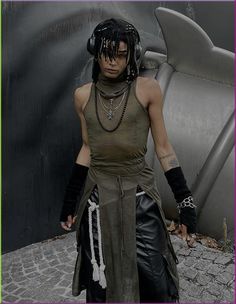 a woman with black hair wearing headphones and leather pants standing in front of a metal sculpture