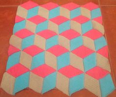 a pink and blue knitted blanket on the floor with tile in the background that looks like hexagons