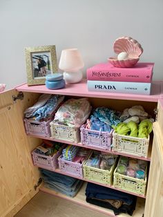 a pink shelf filled with lots of clothes and other items next to a framed photo