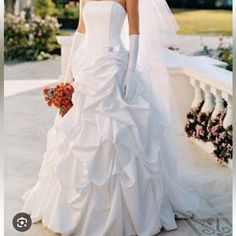 a woman in a white wedding dress and veil standing on a stone wall with flowers