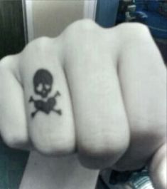 a person's fist with a skull and crossbone tattoo on the middle finger