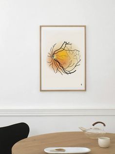 an abstract painting hangs on the wall above a round table in a white walled room