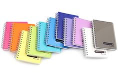 several spiral notebooks lined up next to each other on a white surface with a pen in the middle