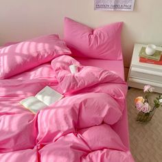 a bed with pink sheets and pillows in a room next to a vase filled with flowers